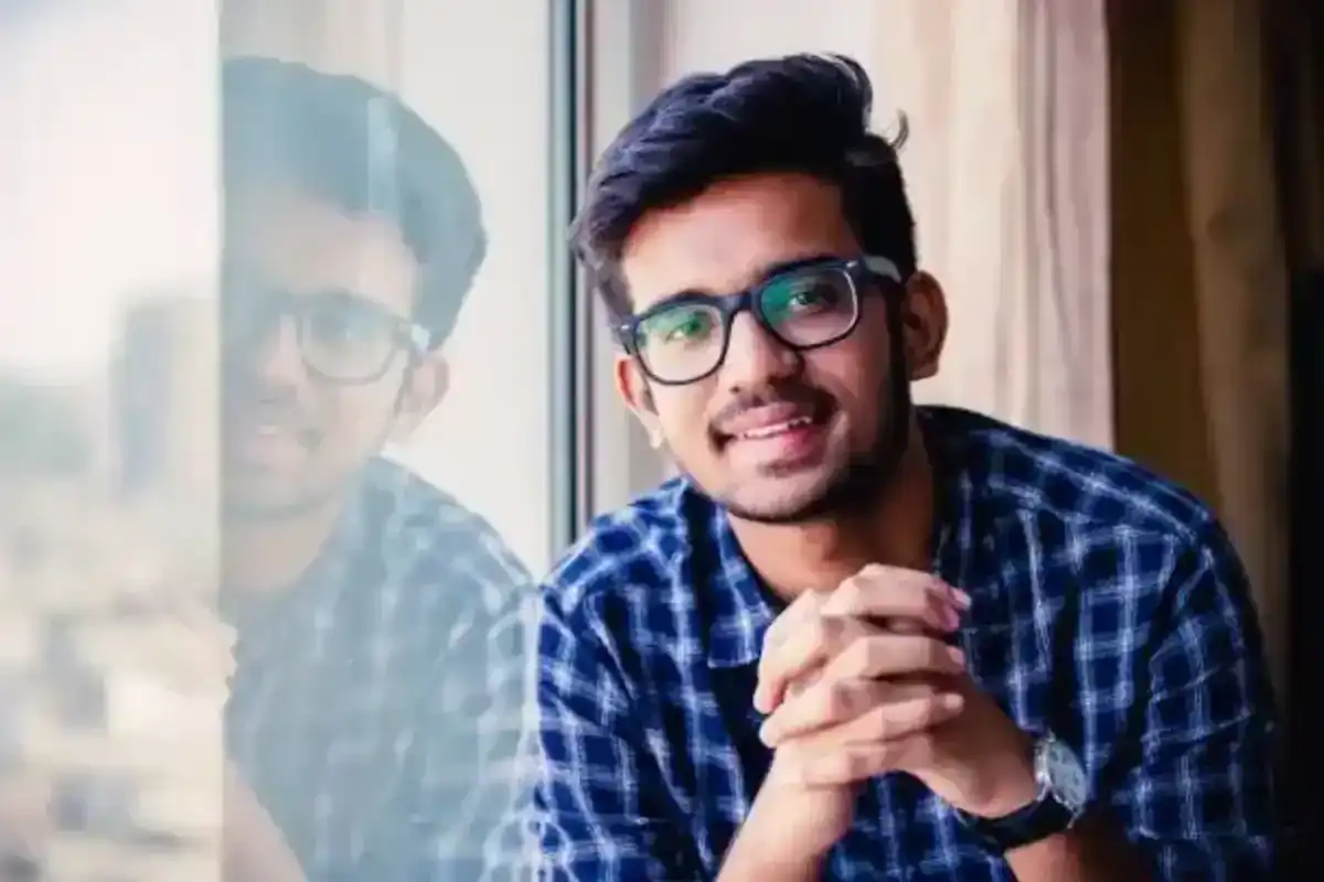 Young Indian man in glasses and blue plaid shirt smiles by window