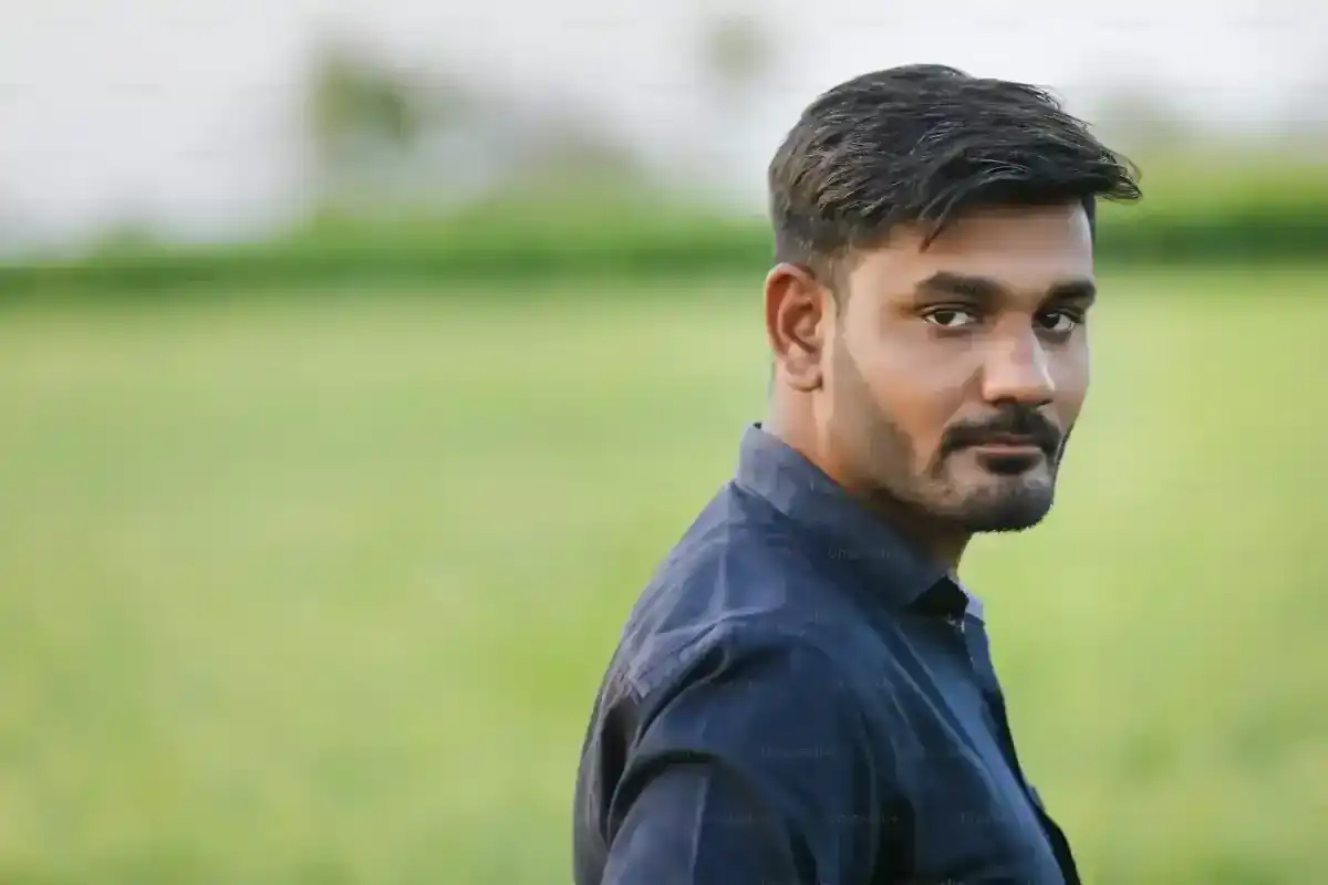 Young Indian man with beard and dark shirt looking to the side in a field