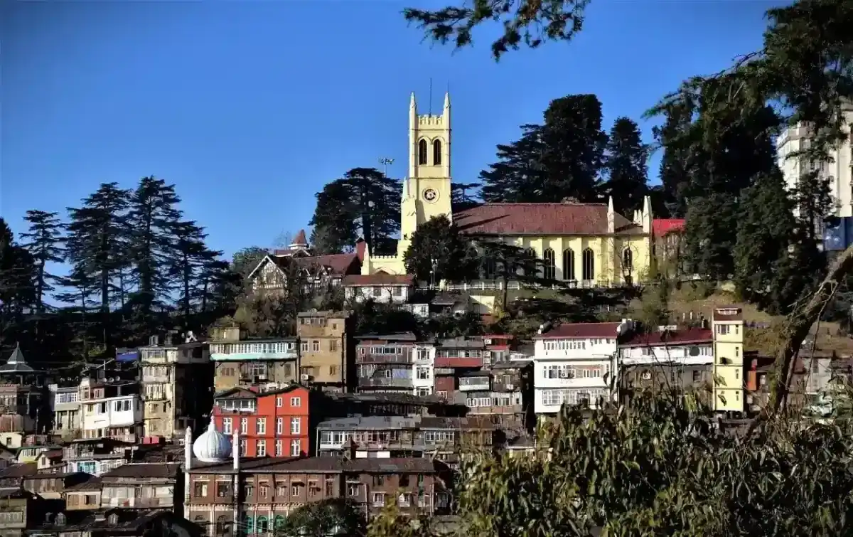 Christ Church Shimla, a prominent yellow church with a clock tower, overlooks a hillside town in India.