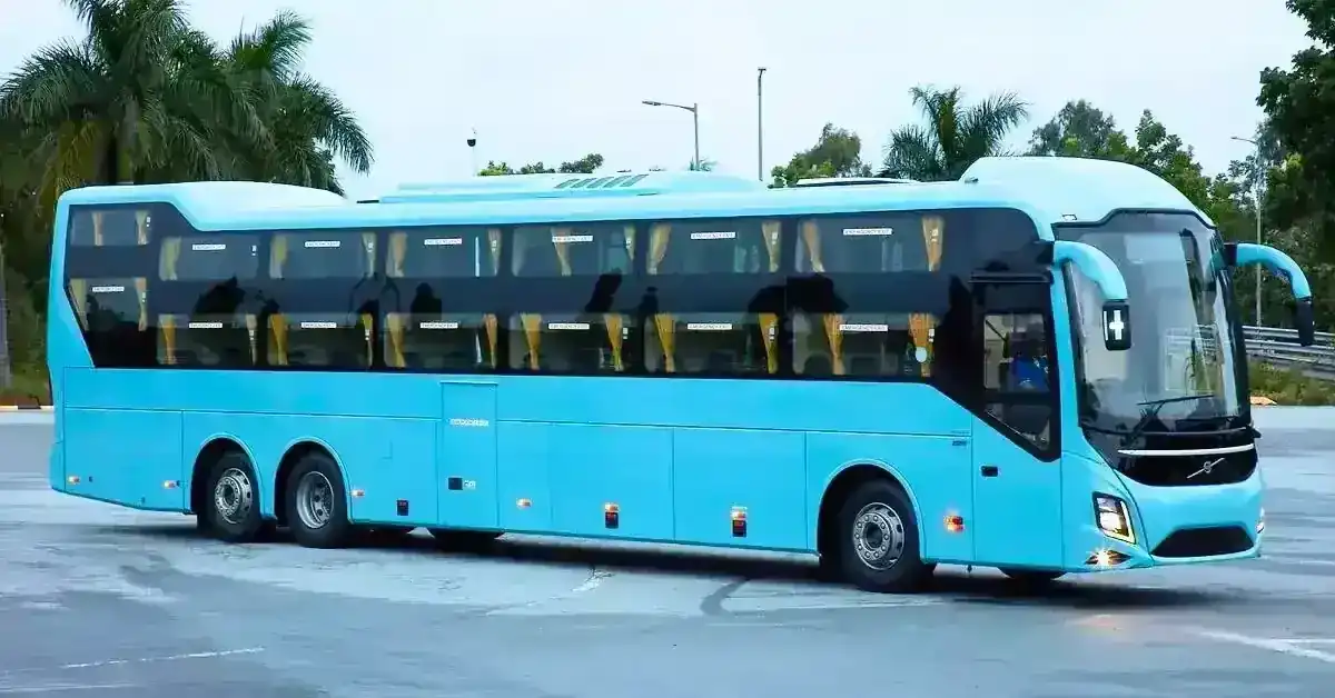 Light blue Volvo bus with multiple windows parked outdoors with palm trees.